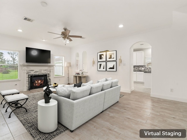 living room with a stone fireplace, ceiling fan, and light hardwood / wood-style floors