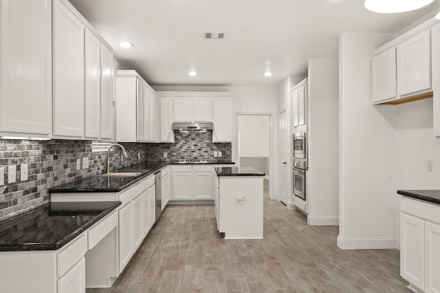 kitchen with under cabinet range hood, stainless steel appliances, a sink, visible vents, and tasteful backsplash