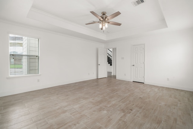 empty room with light wood-style flooring, visible vents, baseboards, a ceiling fan, and a raised ceiling