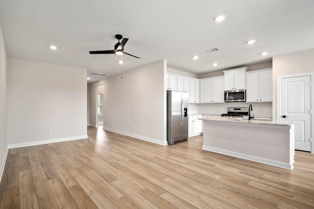 kitchen featuring light wood-type flooring, stainless steel appliances, ceiling fan, a center island with sink, and white cabinets