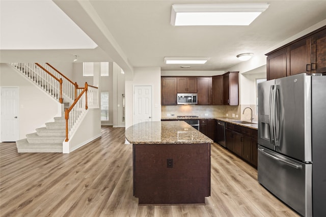 kitchen featuring sink, a center island, light stone counters, dark brown cabinets, and appliances with stainless steel finishes