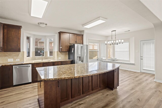 kitchen with a center island, stainless steel appliances, light stone counters, a notable chandelier, and light hardwood / wood-style floors