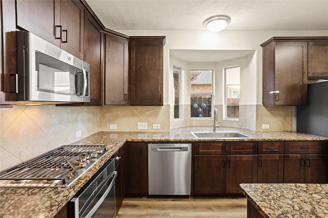 kitchen with appliances with stainless steel finishes, light wood-type flooring, light stone counters, dark brown cabinetry, and sink