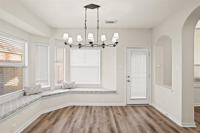 unfurnished dining area with hardwood / wood-style flooring, a wealth of natural light, and an inviting chandelier