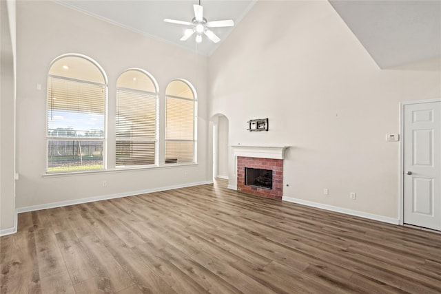 unfurnished living room featuring ceiling fan, hardwood / wood-style floors, high vaulted ceiling, and a brick fireplace