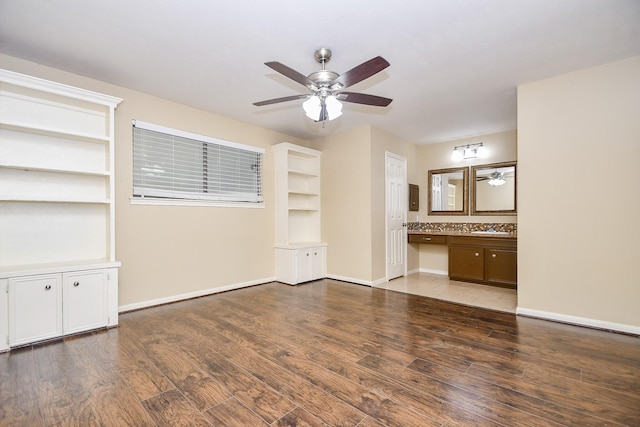 unfurnished living room featuring light wood-style flooring, baseboards, ceiling fan, and built in desk