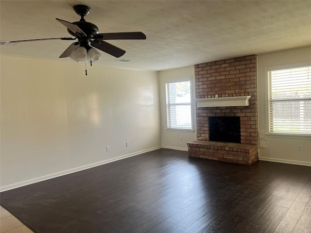 unfurnished living room featuring a brick fireplace, baseboards, dark wood finished floors, and a textured ceiling