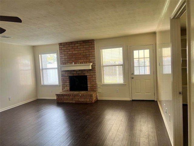 unfurnished living room with a fireplace, visible vents, dark wood-type flooring, a textured ceiling, and baseboards