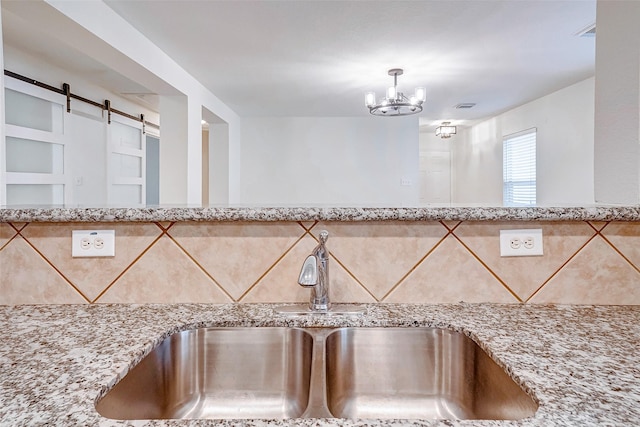 interior details featuring a barn door, light stone countertops, sink, and a notable chandelier