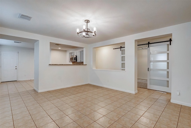 unfurnished room with a barn door, light tile patterned floors, and a chandelier