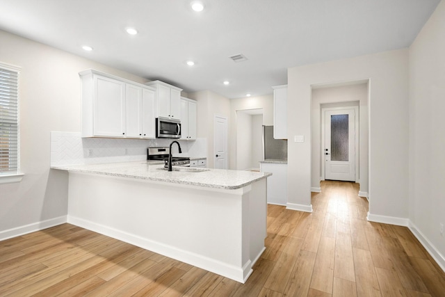 kitchen featuring white cabinetry, sink, kitchen peninsula, appliances with stainless steel finishes, and light wood-type flooring