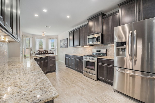 kitchen featuring backsplash, sink, dark brown cabinetry, appliances with stainless steel finishes, and light stone counters