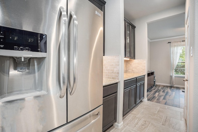 kitchen featuring crown molding, stainless steel refrigerator with ice dispenser, decorative backsplash, and light stone counters