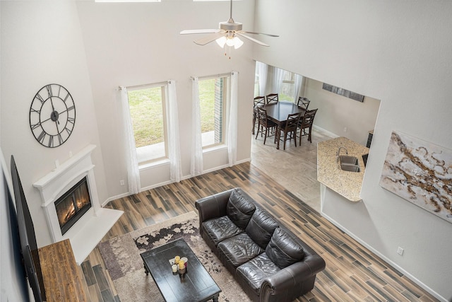 living room featuring ceiling fan, a high ceiling, and wood-type flooring