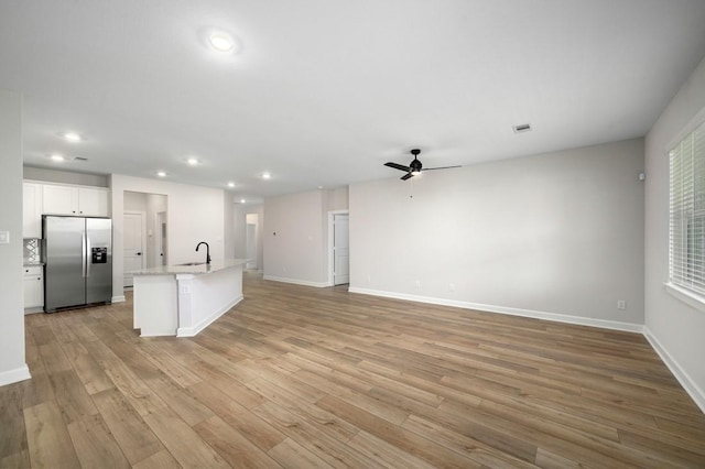 kitchen with white cabinets, sink, stainless steel fridge, an island with sink, and light hardwood / wood-style floors