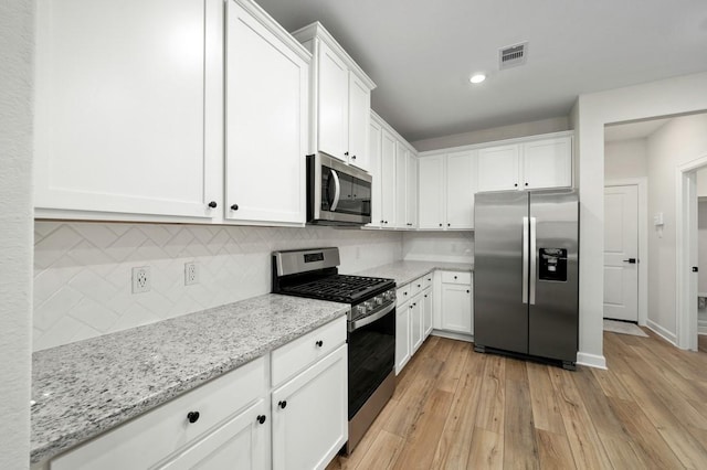 kitchen with white cabinets, light stone countertops, stainless steel appliances, and tasteful backsplash