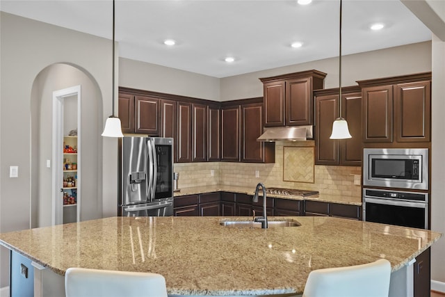 kitchen featuring light stone countertops, sink, stainless steel appliances, and an island with sink