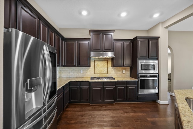 kitchen featuring light stone countertops, dark wood-type flooring, backsplash, dark brown cabinets, and appliances with stainless steel finishes