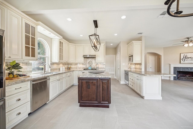 kitchen featuring sink, decorative light fixtures, light stone counters, a kitchen island, and appliances with stainless steel finishes