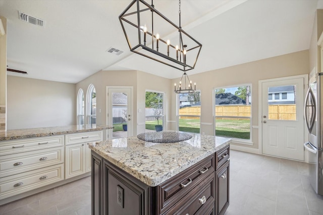 kitchen with decorative light fixtures, light stone countertops, stainless steel fridge, and dark brown cabinetry