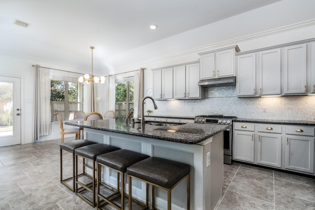 kitchen with stainless steel gas stove, gray cabinets, and a kitchen island with sink