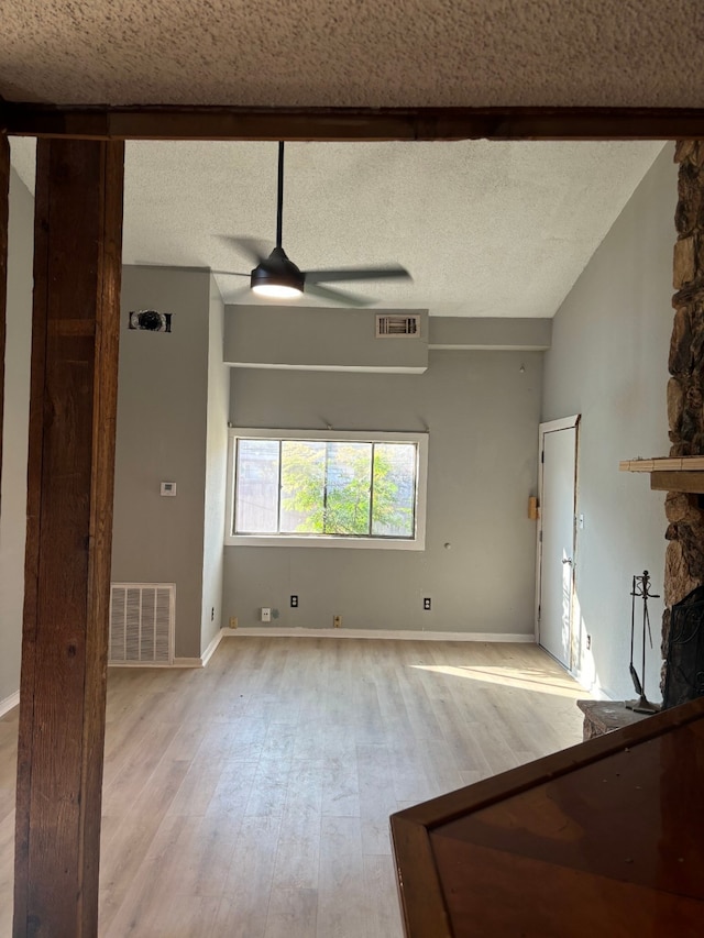 unfurnished room with a textured ceiling, ceiling fan, light hardwood / wood-style floors, and a fireplace