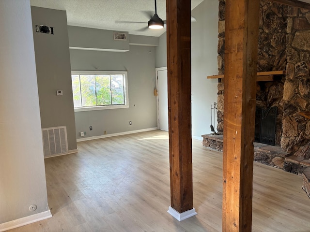 unfurnished room featuring ceiling fan, a fireplace, light hardwood / wood-style floors, and a textured ceiling