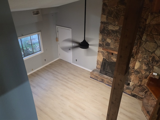 unfurnished living room with vaulted ceiling, light hardwood / wood-style floors, and a stone fireplace