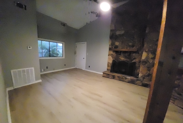 unfurnished living room featuring a stone fireplace, high vaulted ceiling, and wood-type flooring