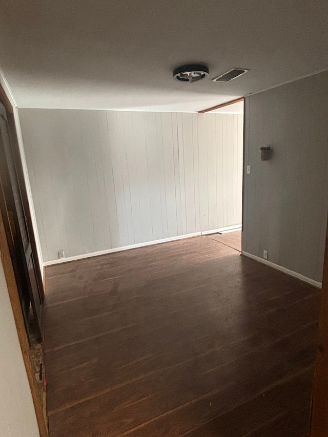 spare room featuring wood walls and dark wood-type flooring