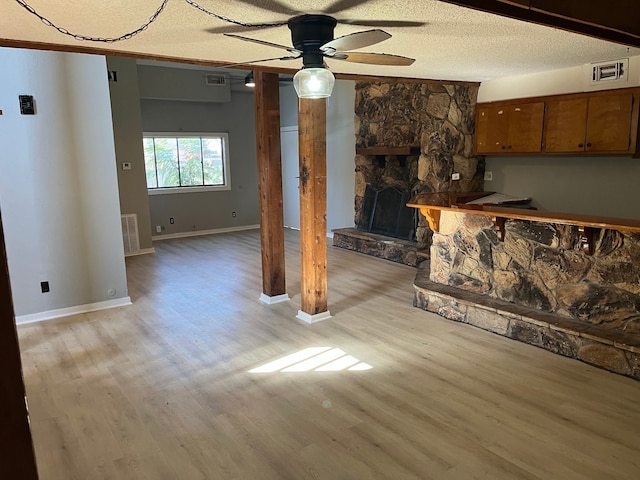 unfurnished living room with a stone fireplace, ceiling fan, light hardwood / wood-style flooring, and a textured ceiling