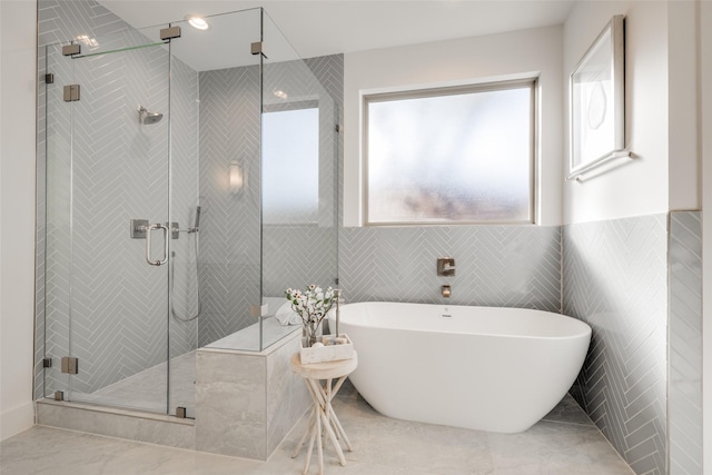 bathroom with shower with separate bathtub and tile walls