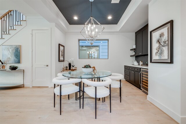 dining area with a tray ceiling, light hardwood / wood-style flooring, beverage cooler, and an inviting chandelier