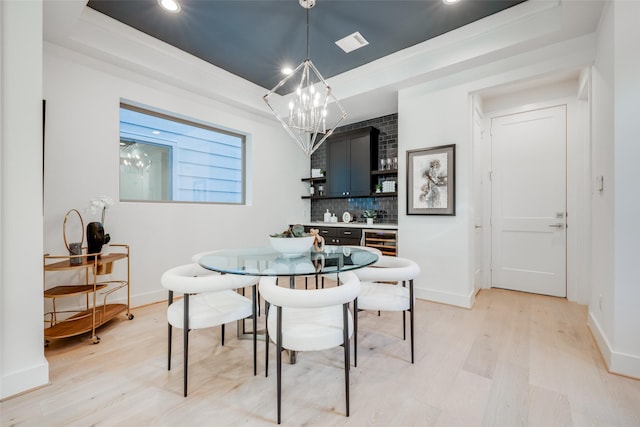 dining room featuring beverage cooler, a chandelier, light hardwood / wood-style floors, a tray ceiling, and ornamental molding