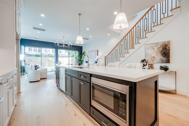 kitchen with white cabinetry, stainless steel microwave, sink, decorative light fixtures, and a kitchen island with sink