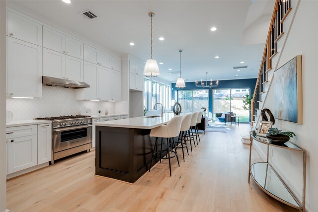 kitchen featuring a kitchen island with sink, decorative light fixtures, light hardwood / wood-style flooring, white cabinets, and stainless steel stove