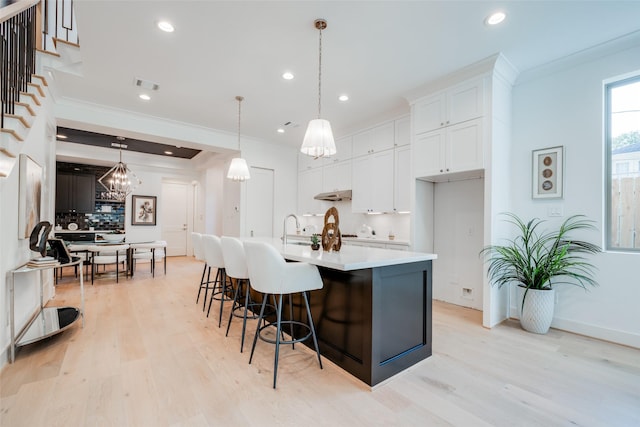 kitchen featuring pendant lighting, backsplash, ornamental molding, an island with sink, and white cabinetry