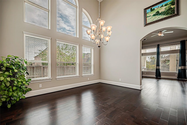 spare room with ceiling fan with notable chandelier, dark hardwood / wood-style floors, and a towering ceiling