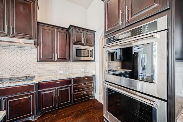 kitchen with decorative backsplash, appliances with stainless steel finishes, light stone countertops, dark brown cabinets, and dark hardwood / wood-style floors