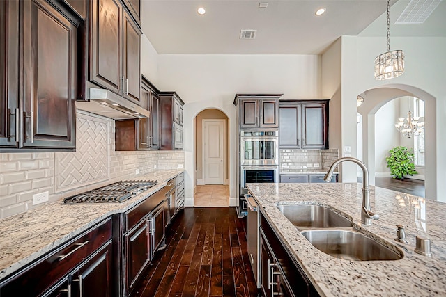 kitchen with dark brown cabinetry, sink, hanging light fixtures, range hood, and appliances with stainless steel finishes