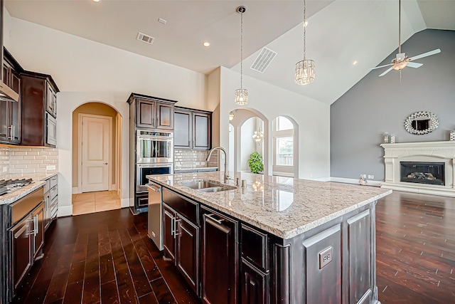 kitchen featuring backsplash, dark brown cabinetry, sink, and a center island with sink