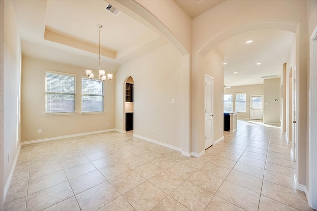 spare room featuring ceiling fan with notable chandelier, light tile patterned flooring, and a raised ceiling