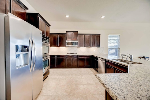 kitchen with light stone countertops, kitchen peninsula, stainless steel appliances, sink, and light tile patterned floors