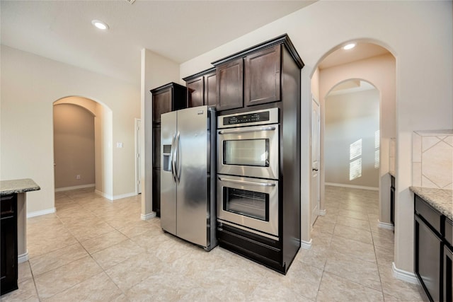 kitchen featuring light tile patterned floors, light stone counters, dark brown cabinetry, and appliances with stainless steel finishes