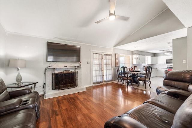 living room with lofted ceiling, hardwood / wood-style flooring, ceiling fan with notable chandelier, and a brick fireplace