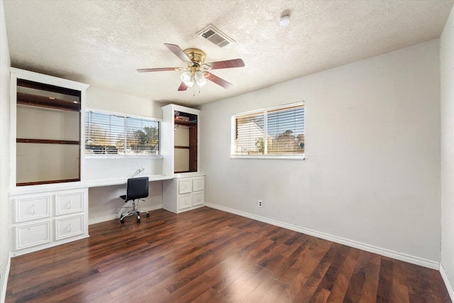 unfurnished office featuring a textured ceiling, ceiling fan, built in desk, and dark wood-type flooring