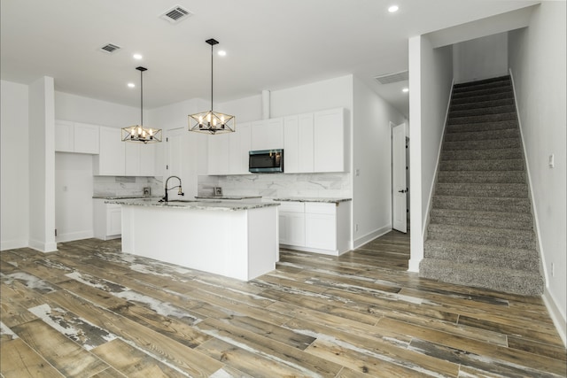 4702 Ward, Houston, TX 77021 - kitchen featuring stainless steel microwave, a chandelier, wood-type flooring, white cabinets, and backsplash