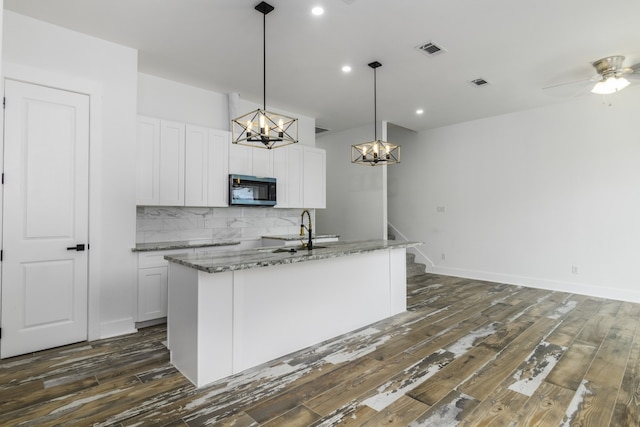 kitchen featuring pendant lighting, a center island with sink, ceiling fan, dark stone countertops, and white cabinetry