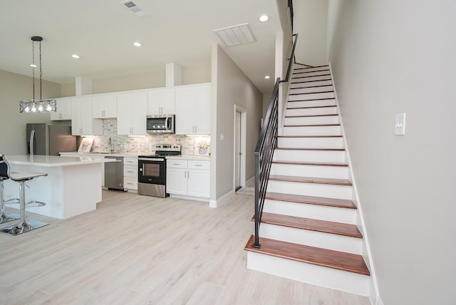 kitchen with decorative backsplash, appliances with stainless steel finishes, a center island, white cabinetry, and hanging light fixtures