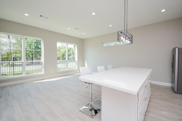 kitchen featuring pendant lighting, a center island, white cabinets, a kitchen breakfast bar, and stainless steel fridge